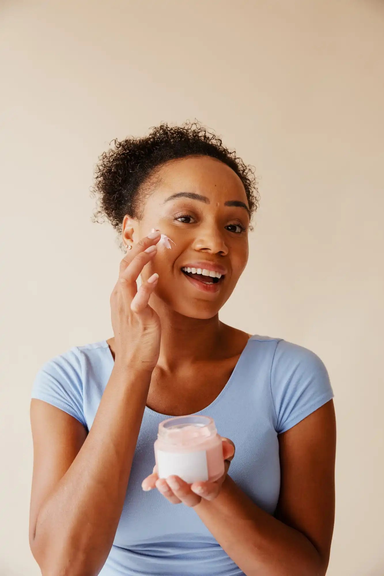 Smiling woman applying facial cream to her cheek